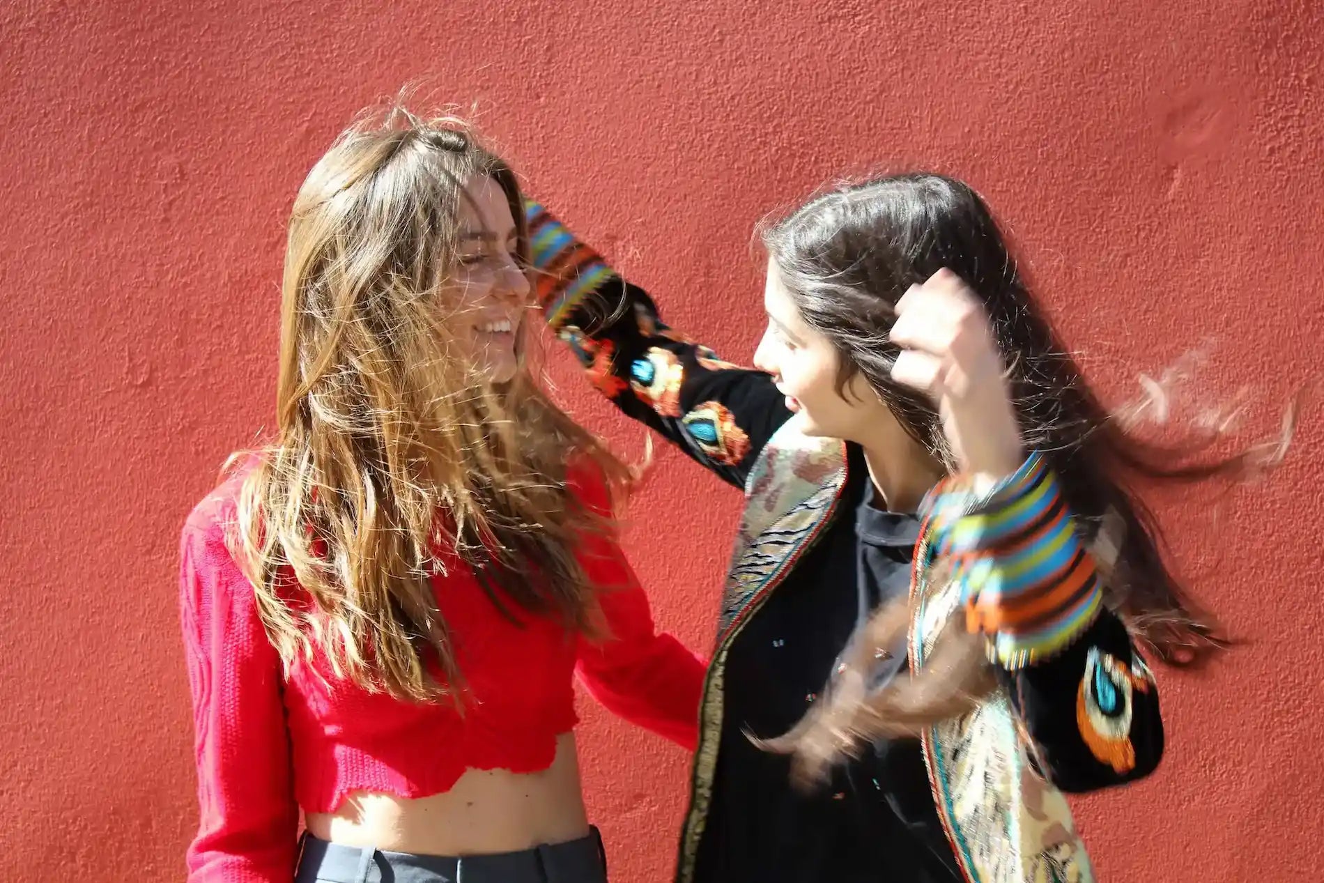 Two girls laughing in front of a red wall. wearing patrick owen and laure welfling limited collection for boutique kaotique 
