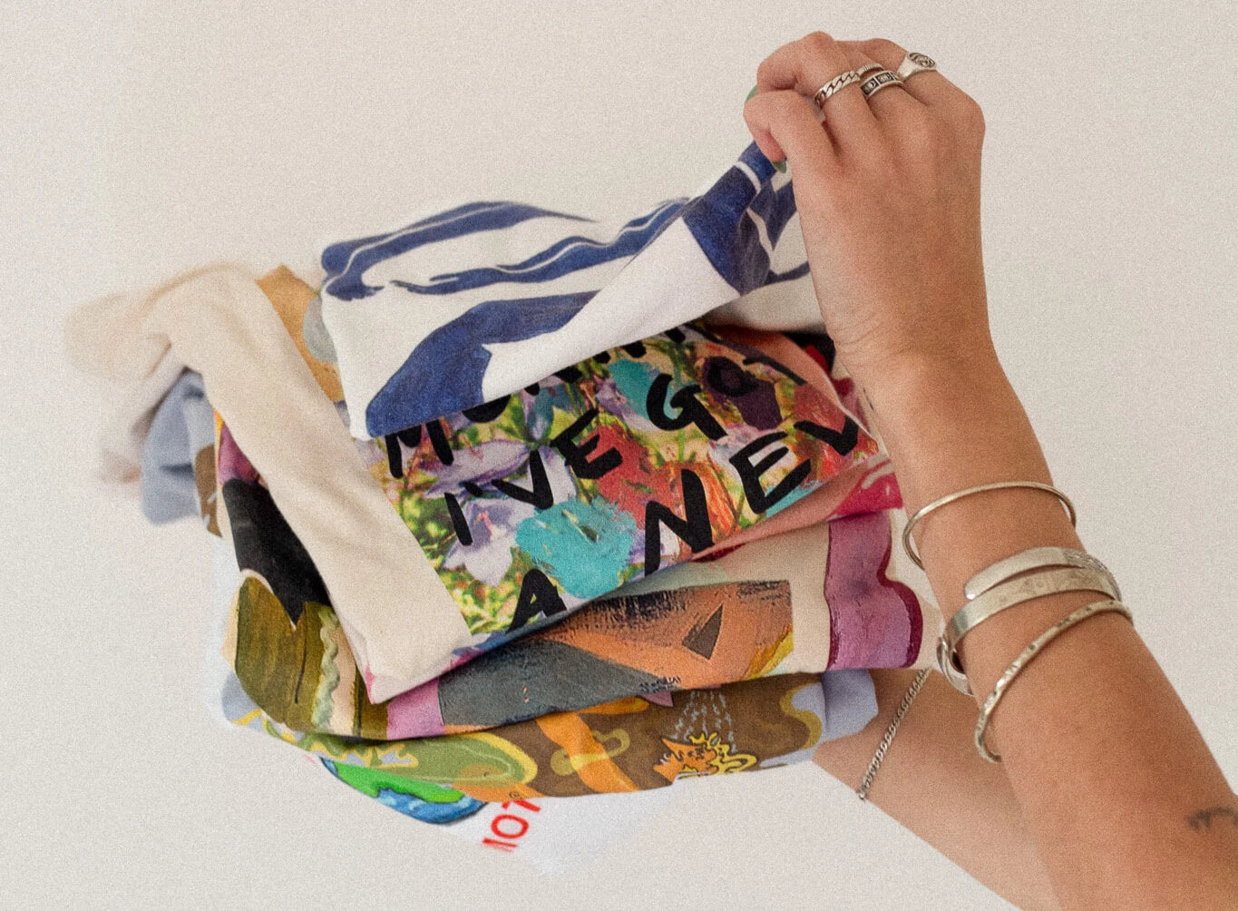 Hand holding a stack of colorful folded organic cotton boutique kaotique graphic t-shirts against a white background