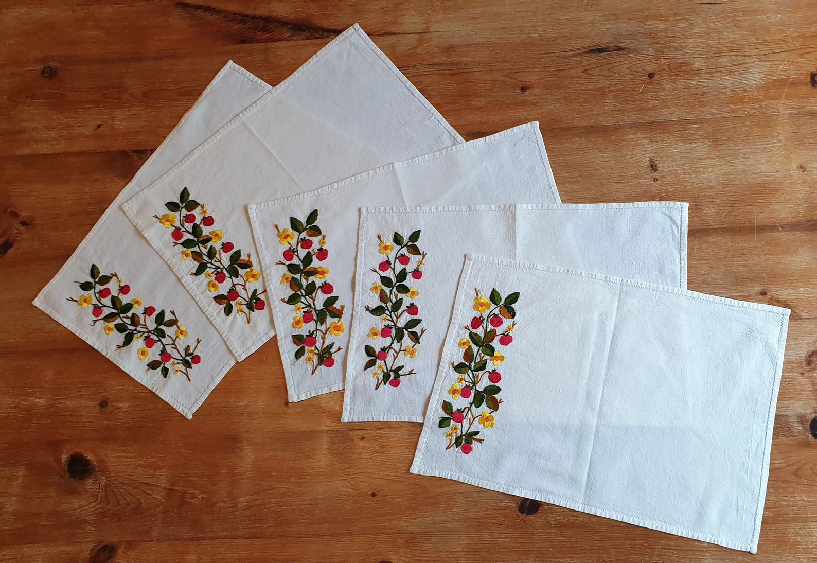 Set of embroidered placemats with floral patterns on a wooden surface. PLATE MAT WITH STRAWBERRies 