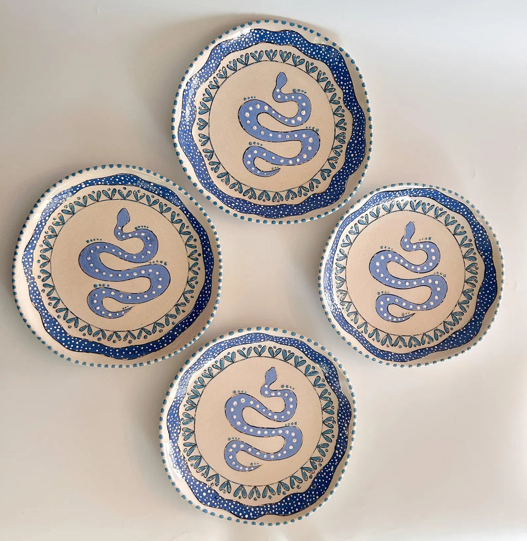 Four ceramic plates with blue snake designs on a beige background