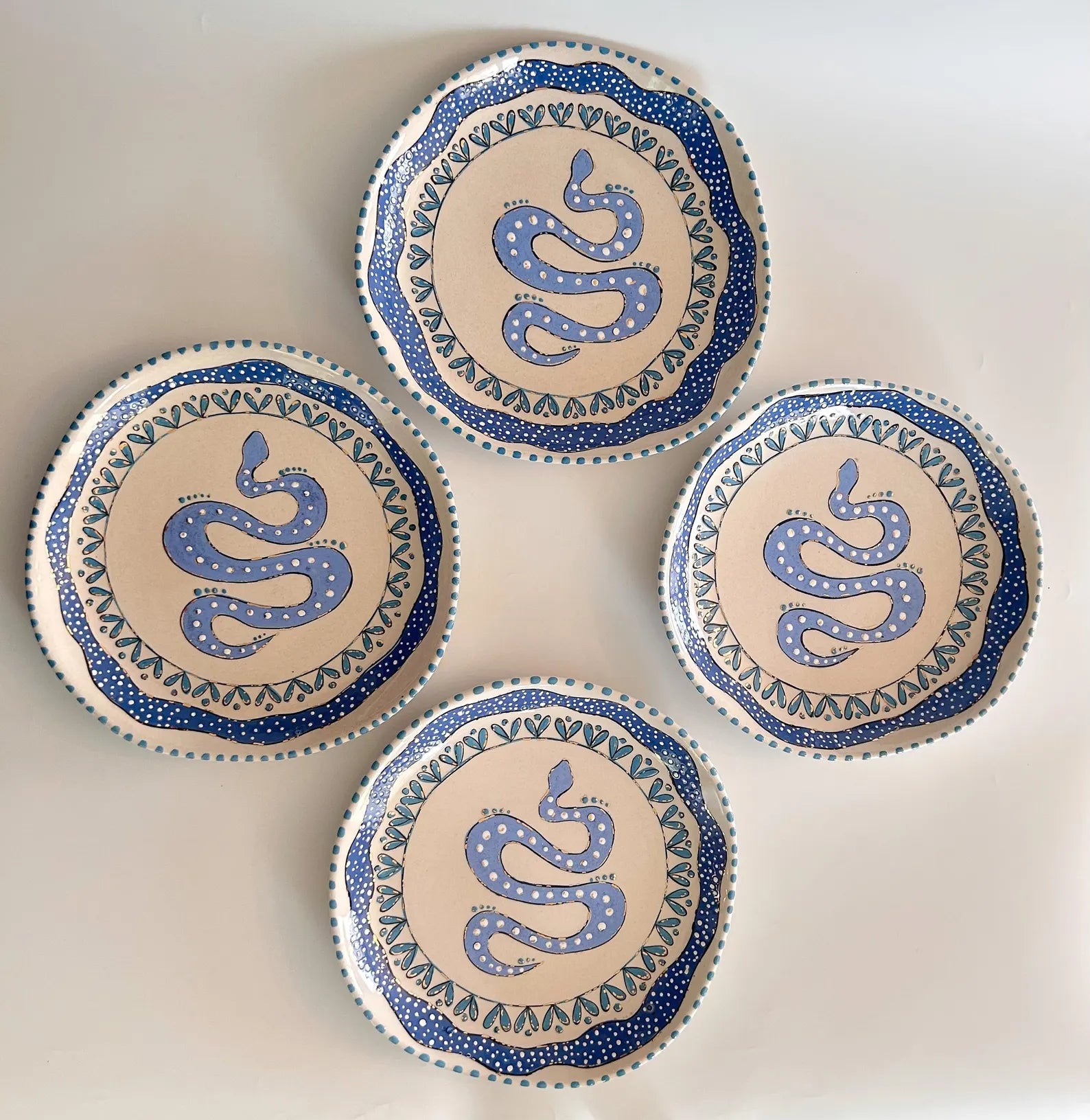 Four ceramic plates with blue snake designs on a beige background