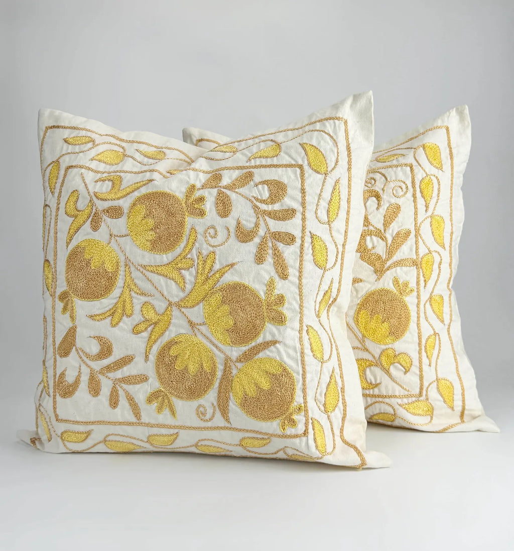 Two decorative pillows with gold floral patterns on a white background