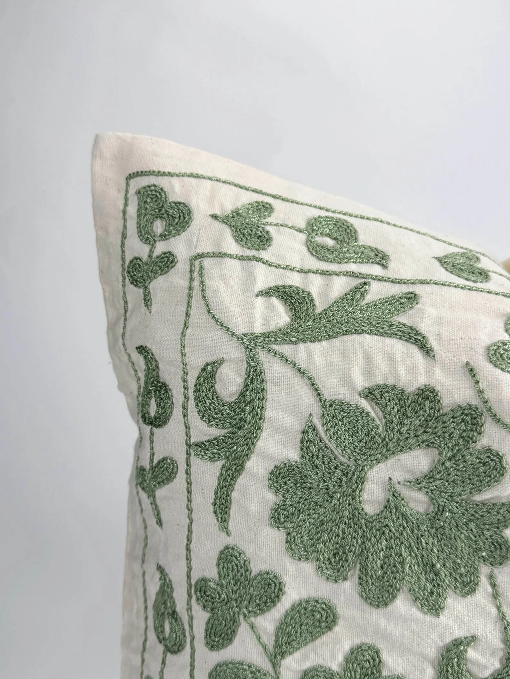 Decorative pillow with green floral embroidery on a white background