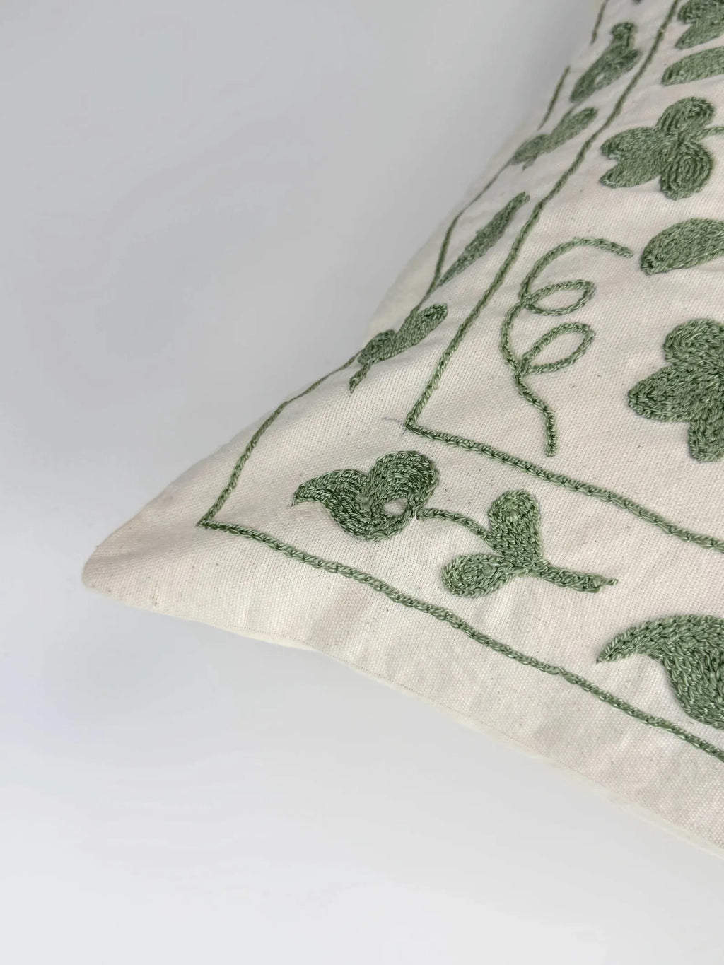 Decorative pillow with green floral embroidery on a white background