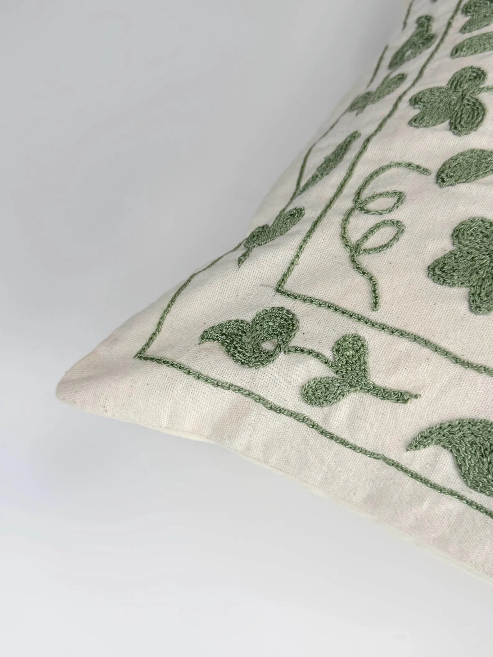 Decorative pillow with green floral embroidery on a white background