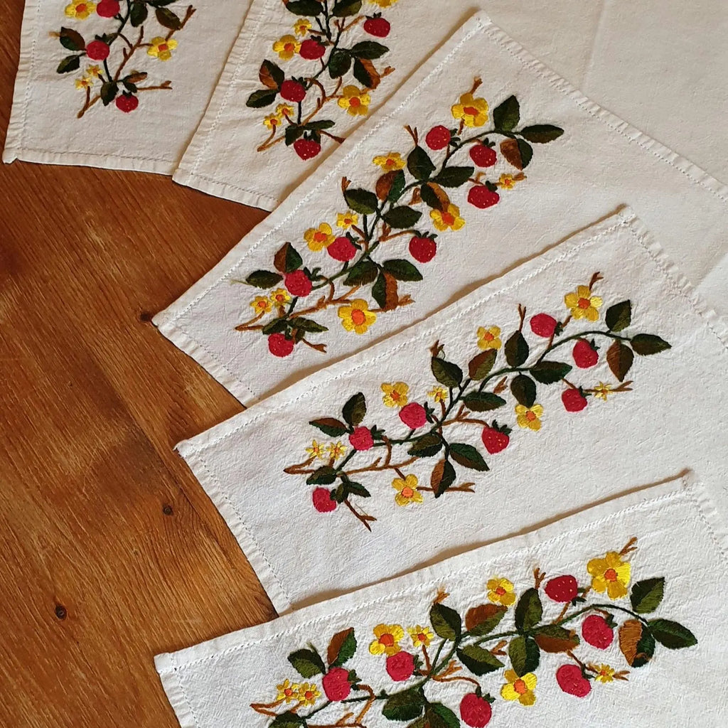 Set of embroidered placemats with floral patterns on a wooden surface. PLATE MAT WITH STRAWBERRies 