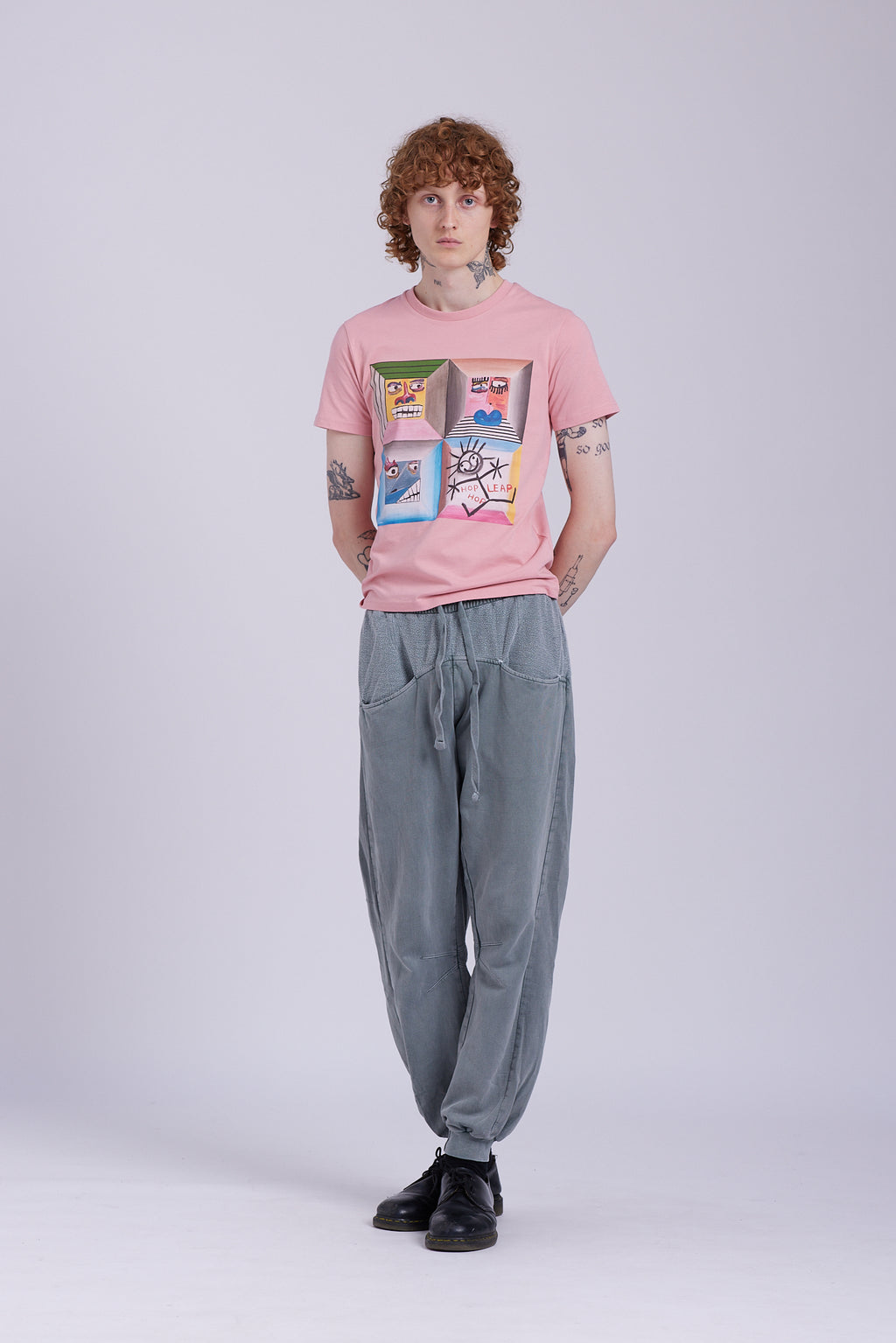 An organic cotton t-shirt in rose clay color with a graphic print of four different characters in a grid layout. Four Moods affirmation tee — rose clay organic cotton t-shirt with painted mood print, unisex fit, mental health charity