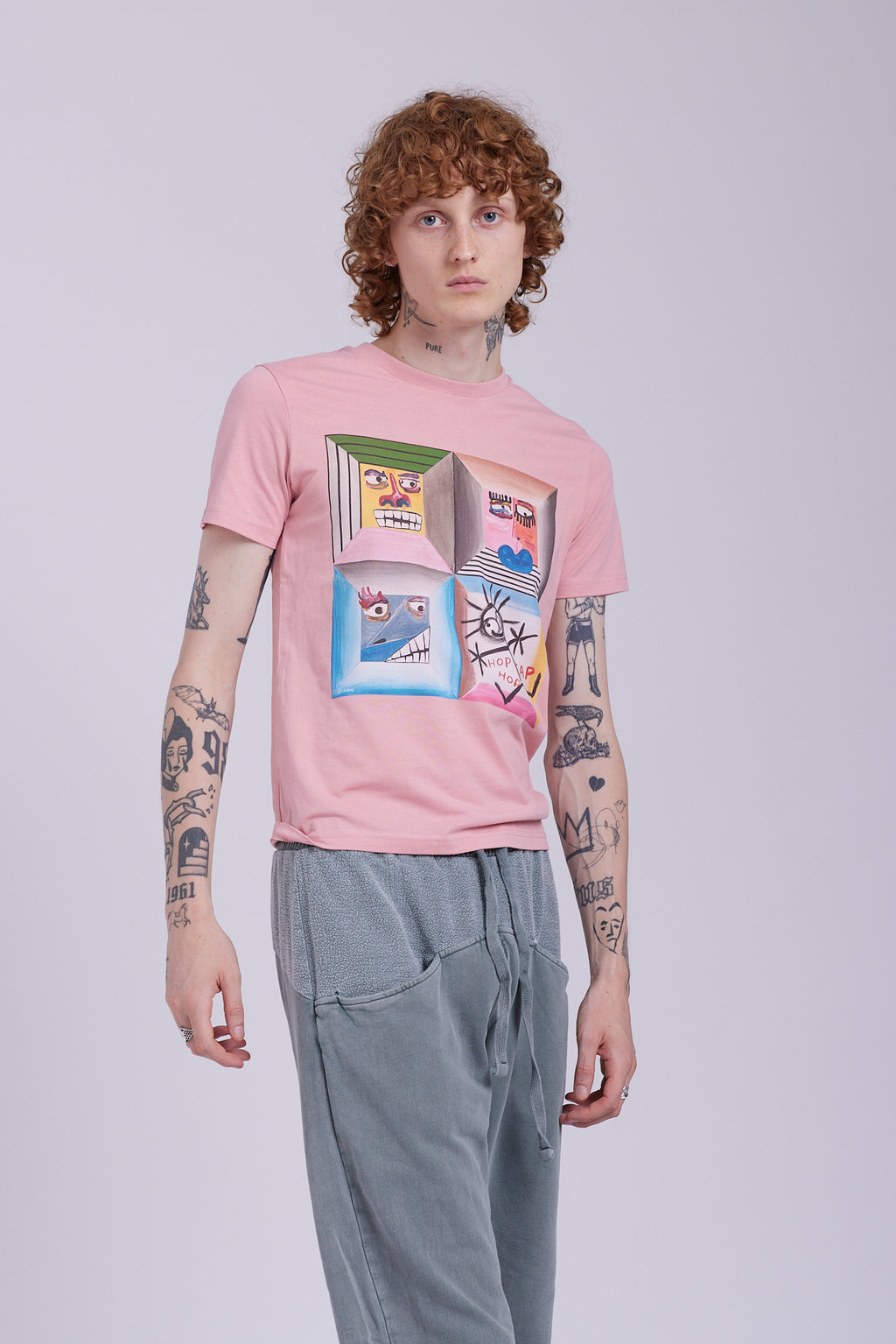 An organic cotton t-shirt in rose clay color with a graphic print of four different characters in a grid layout. Four Moods affirmation tee — rose clay organic cotton t-shirt with painted mood print, unisex fit, mental health charity